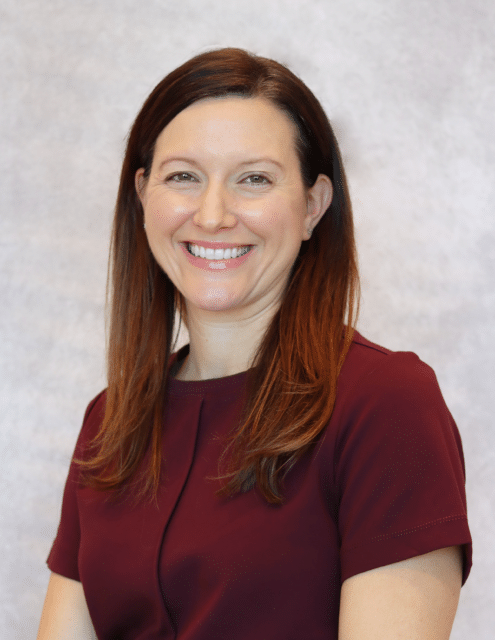 Allyson Naylor smiling while wearing a maroon blouse against a light background.
