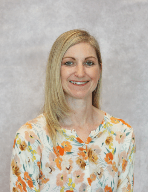 Tracy Luther, APRN-C, smiling with blonde hair, wearing a floral shirt against a gray background.