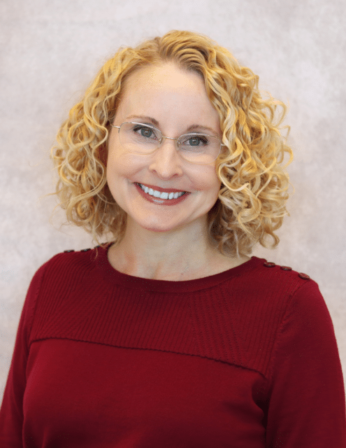 Teresa Truman, APRN-C, smiling with curly blonde hair and wearing a red sweater.